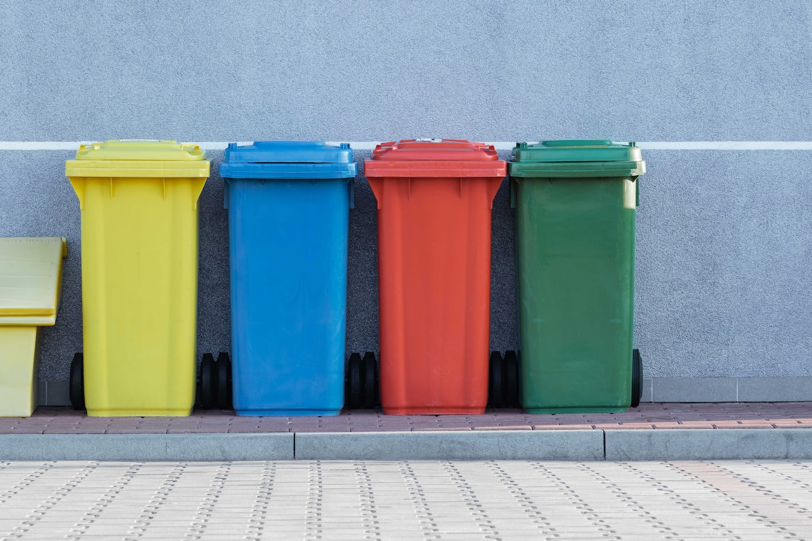 Four colorful recycling trashbins in front of a grey wall