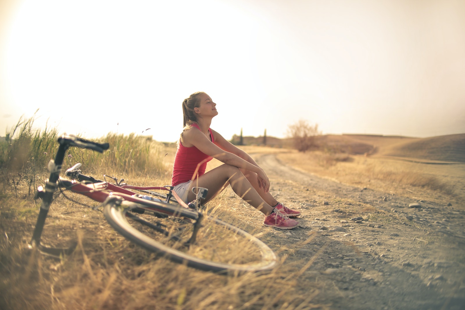 Woman sitting on the side of the road under the sun next to her bike