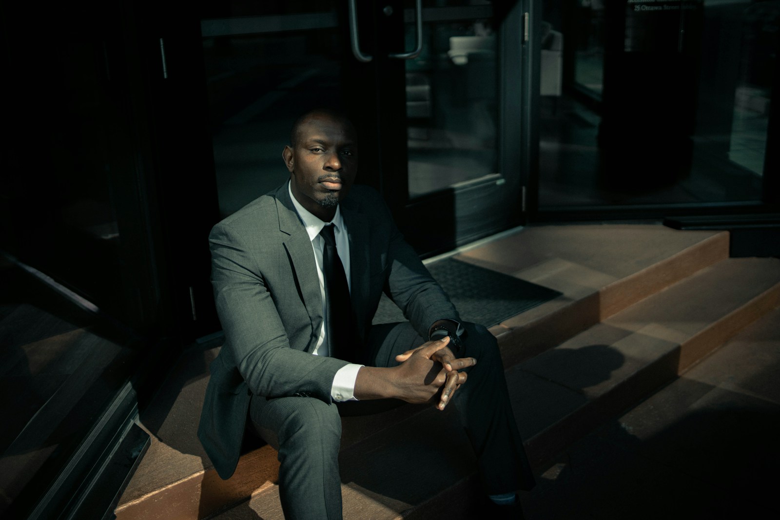 man in black suit sitting on brown wooden bench