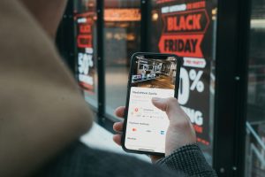 person holding black smartphone in front of black friday shopwindow